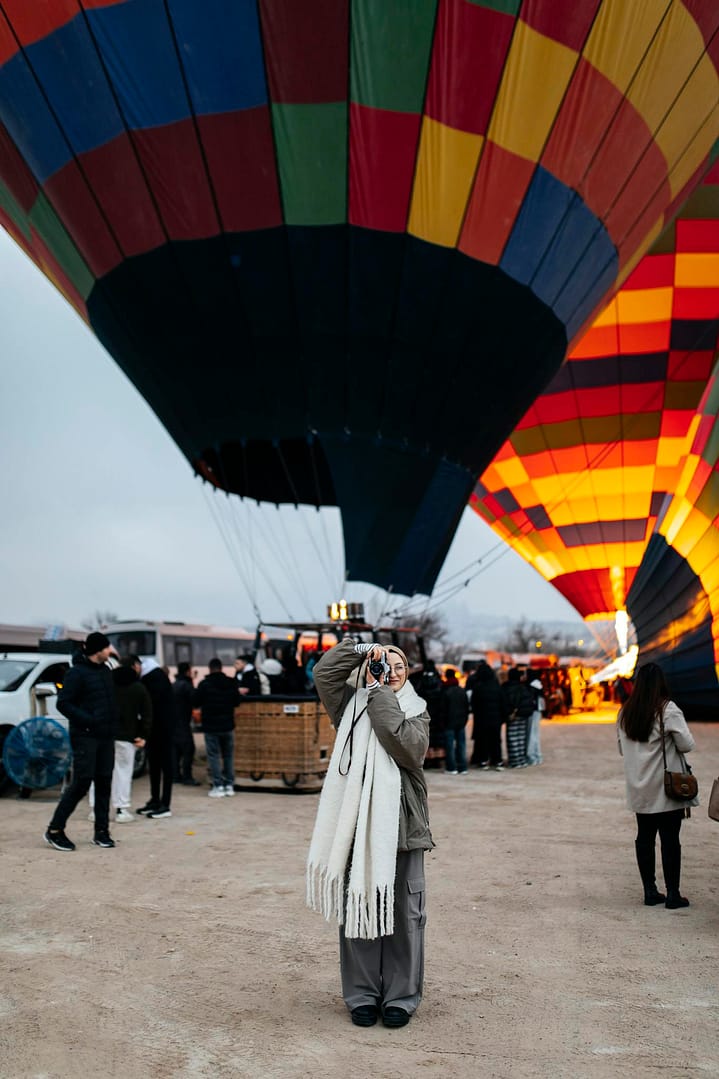 A woman photographs colorful hot air balloons at a launch site in Cappadocia, Turkey.