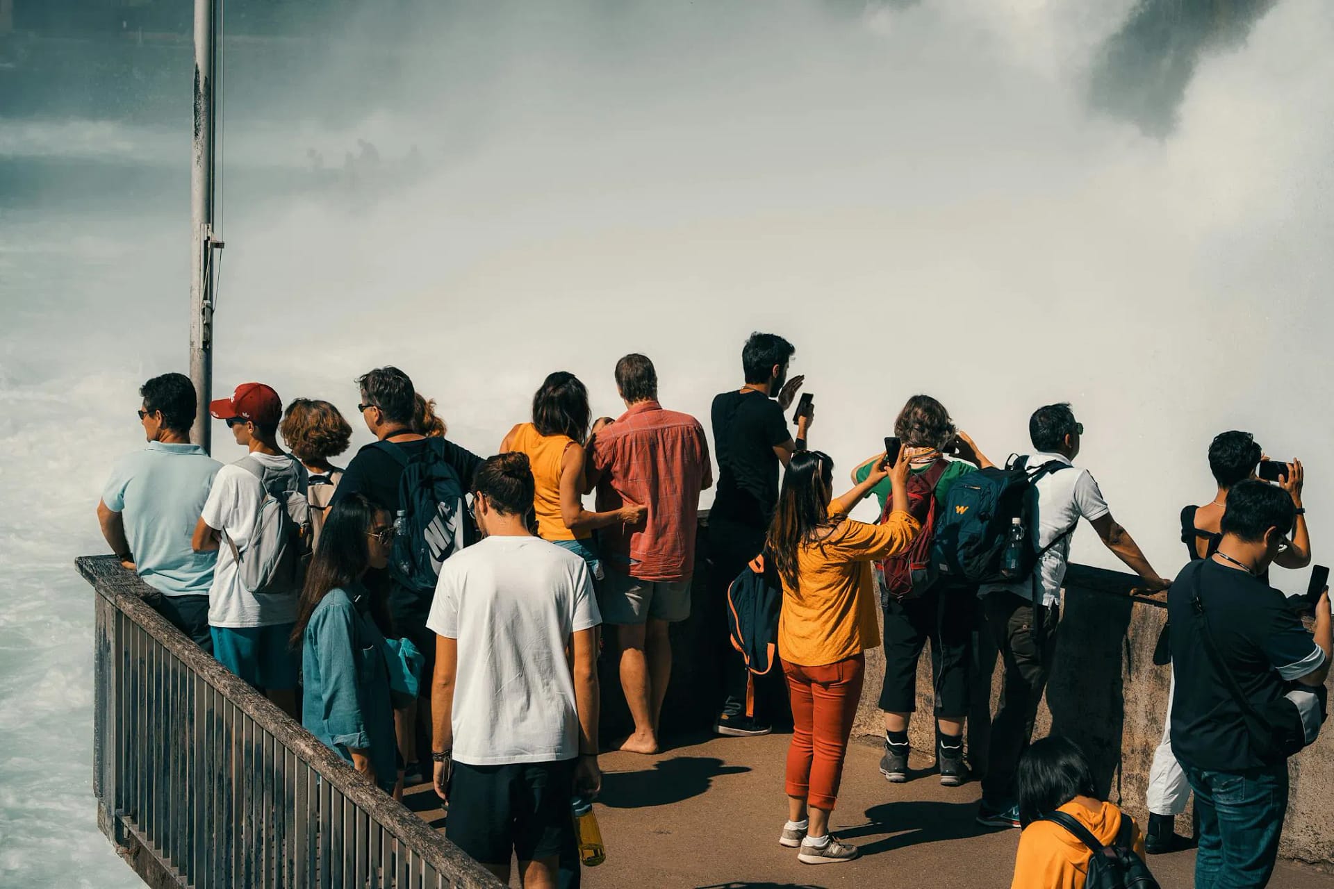 Group of tourists capturing the majestic Rhine Falls from a viewing platform in Switzerland.